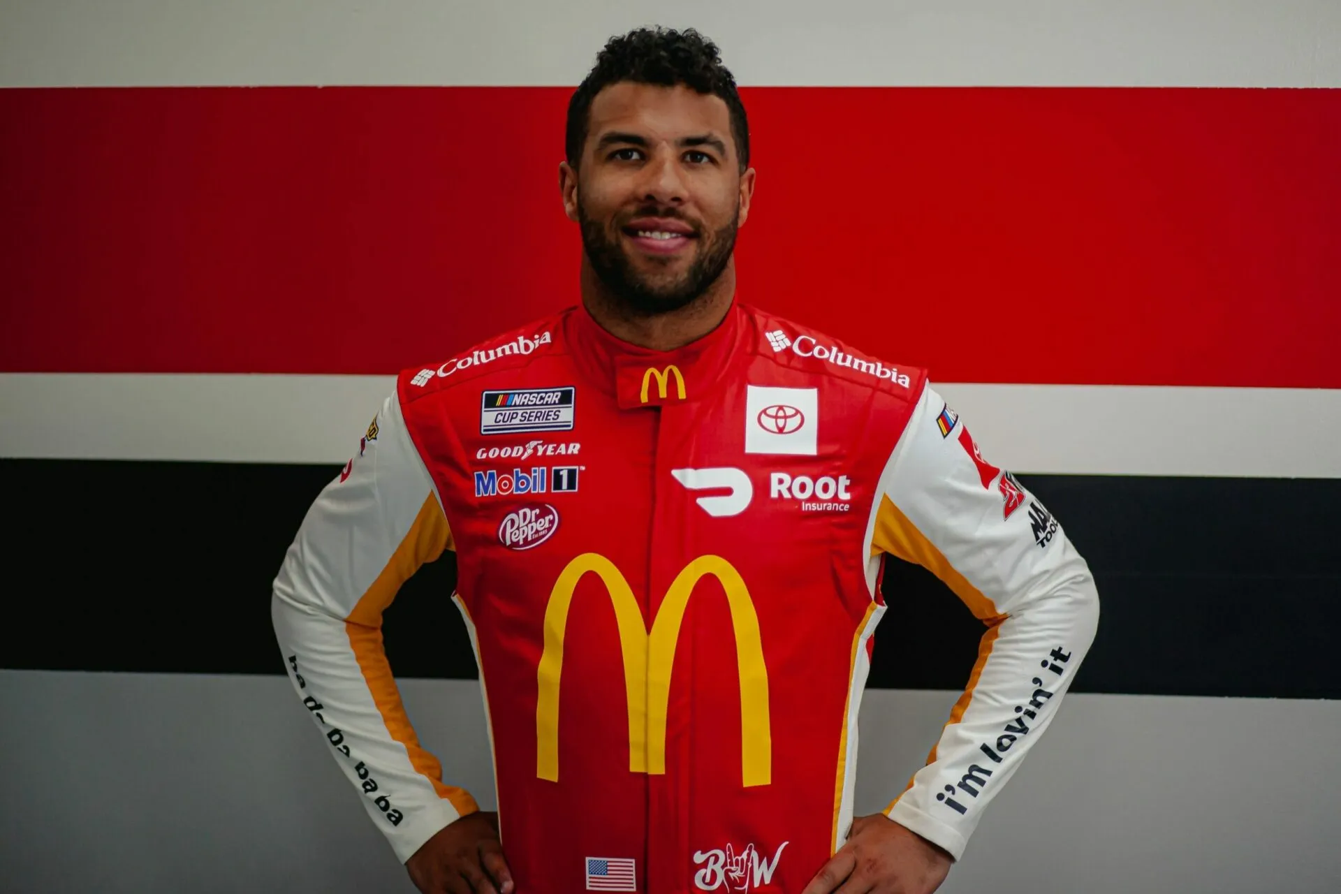 A man in red and white racing suit standing next to a wall.